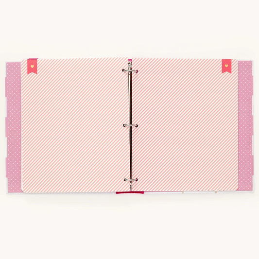 A three-ring binder with pink and white patterned pages, featuring diagonal stripes on the main pages, polka dots on the side flaps, and small red heart-shaped tabs on the top corners.