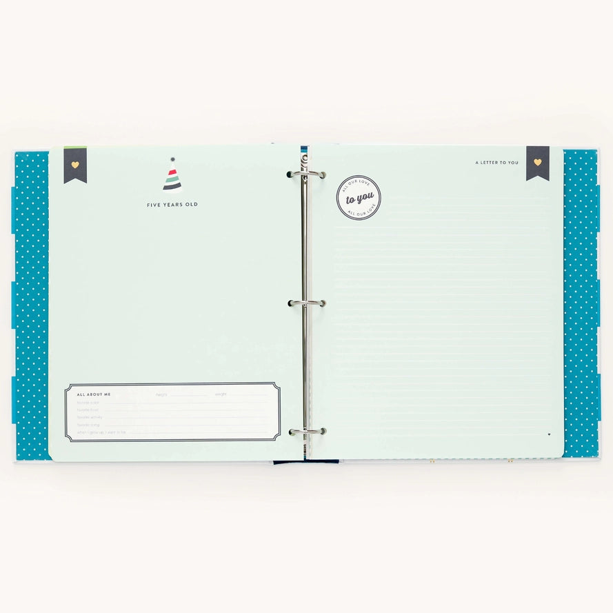 An open ring-bound planner or album with pale mint pages, teal polka-dot side panels, and printed stationery inserts, photographed against a plain white background.