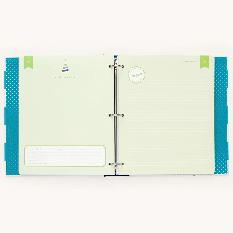 An open three-ring binder planner or agenda with pale green lined pages, teal polka-dot side panels, and small decorative printed details on the pages, shown against a plain light background.