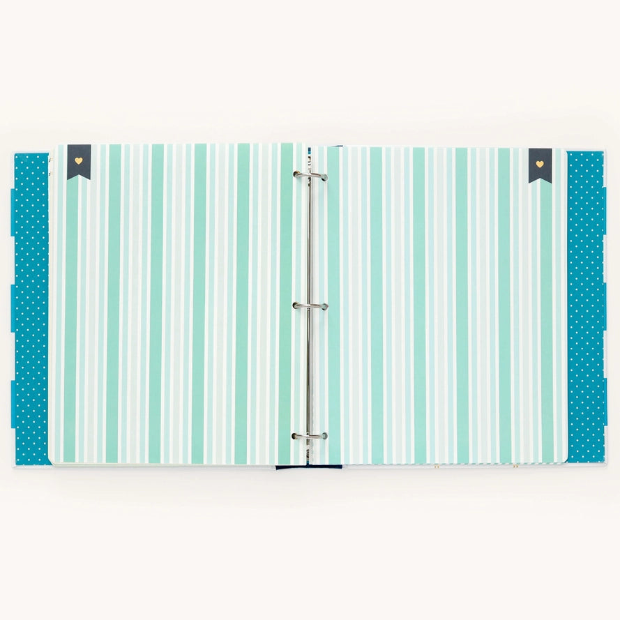 A three-ring binder with a striped cover in shades of mint green, teal, and white, featuring solid teal polka-dot side tabs and small dark gray decorative end tabs with gold hearts.