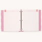 A three-ring binder planner or album shown open, displaying pink and white striped divider pages with pink polka-dot borders and ribbon tabs.