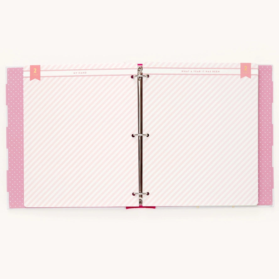 A three-ring binder planner or album shown open, displaying pink and white striped divider pages with pink polka-dot borders and ribbon tabs.