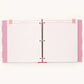 A three-ring binder notebook with white textured pages, pink patterned side covers, and a silver metal ring closure, shown against a plain off-white background.
