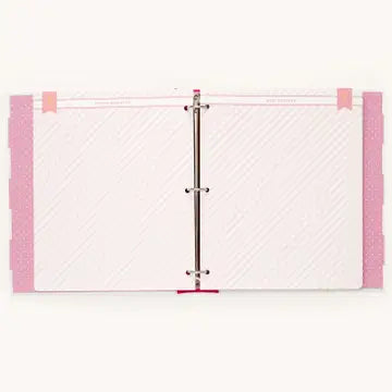 A three-ring binder notebook with white textured pages, pink patterned side covers, and a silver metal ring closure, shown against a plain off-white background.