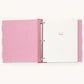 A pink ring binder notebook with a textured patterned cover, open to a white page with the word 'Baby' written in pink script.