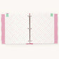 An open three-ring binder notebook with white pages decorated with small pink and green polka dots, pink patterned side tabs, and mint green bookmark tabs on a light cream background.