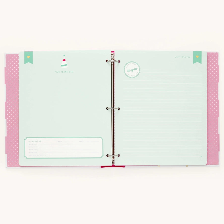 An open three-ring binder planner or notebook showing pastel mint green interior pages with pink patterned side tabs and a silver metal ring closure.