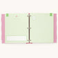 An open three-ring binder planner or agenda with pale green lined pages, pink polka-dot side tabs, and small decorative printed details, photographed on a plain light background.